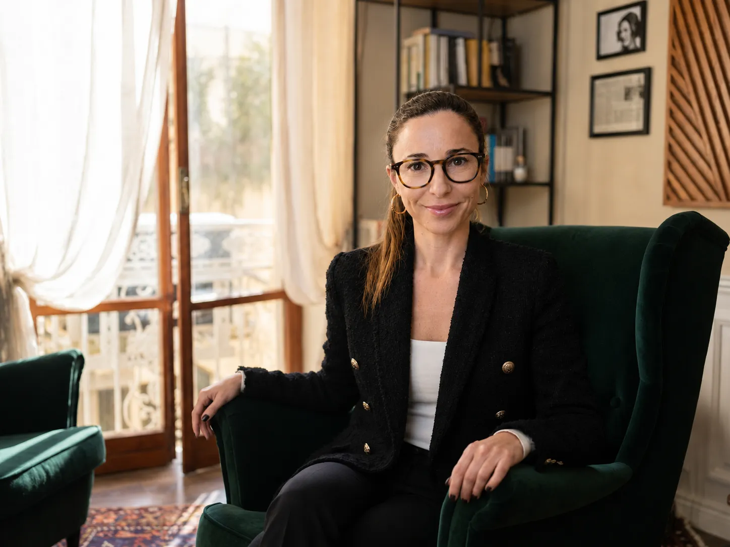Dott.ssa Laura Castaldo seduta su una poltrona verde nel suo studio a Napoli, con finestra luminosa e libreria sullo sfondo.